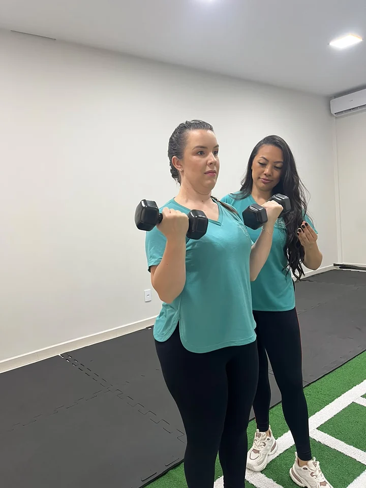 Duas fisioterapeutas fazem exercício de bíceps com halteres na sala de treino