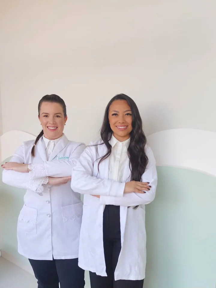 Dra. Rafaela Rigo e Kalyne Tomas, de jaleco, na sala de espera da Saluthe
