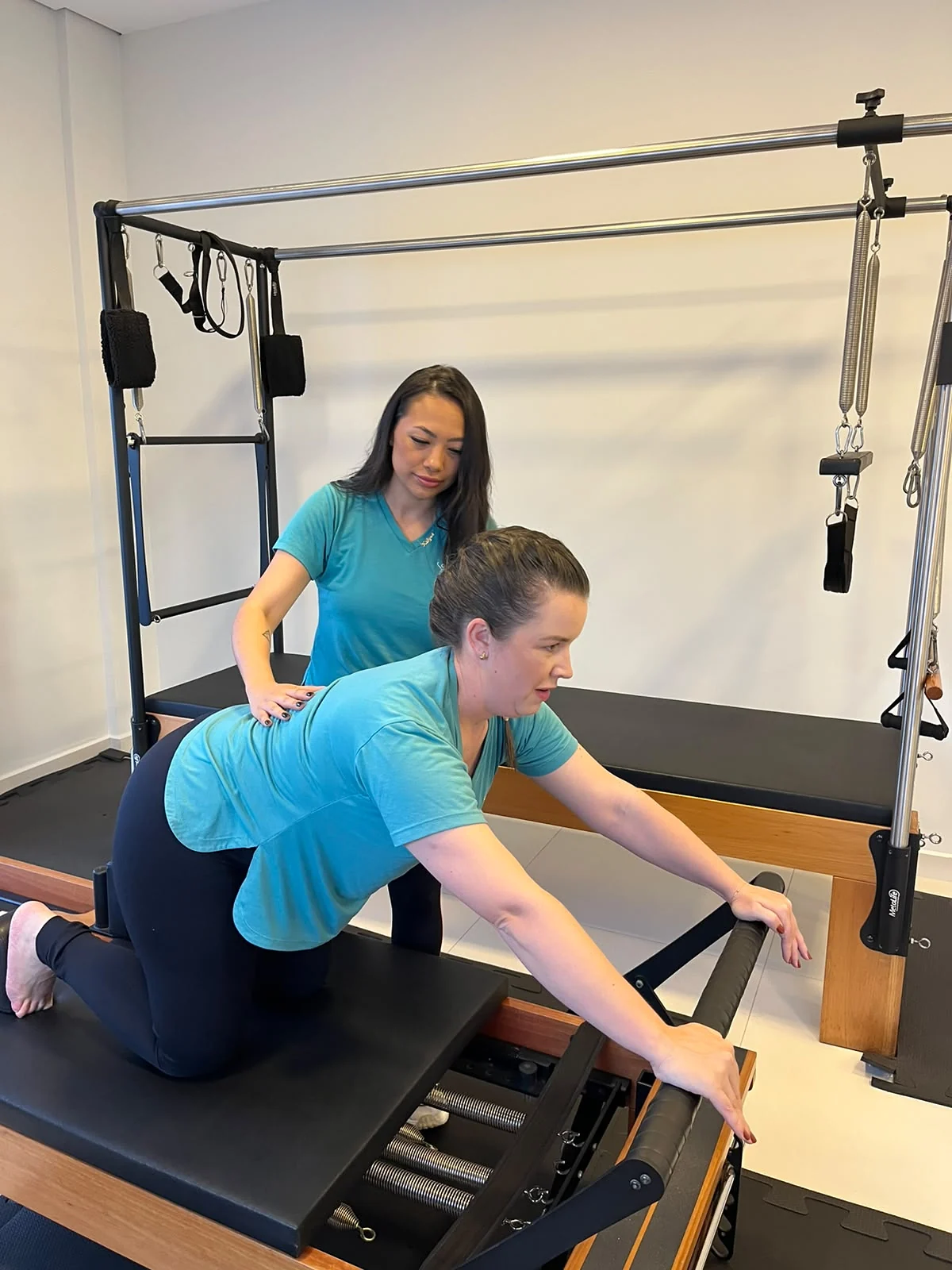 Fisioterapeuta ajusta a postura de uma aluna ajoelhada no cadillac de Pilates